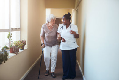 Senior woman with walking stick being helped by a female nurse
