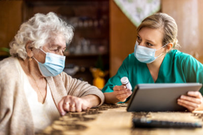 Female nurse reviewing prescription bottle with senior woman